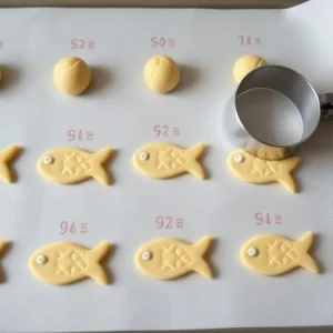 Once the dough is ready, use a spoon or cookie scoop to grab small portions of dough. Roll them into balls and place them on the prepared baking sheet, leaving a little space between each cookie.To create the fish shape, you can either use a fish-shaped cookie cutter or mold the dough by hand into fish shapes. Be creative and make each fish unique!